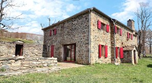 Un bâtiment en pierre avec des volets rouges, un escalier en pierre et une zone herbeuse.