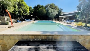 Une piscine rectangulaire à l’eau d’un bleu limpide, entourée de chaises longues et d’un mur de pierre.