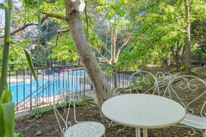 A poolside area with metal chairs and a table, surrounded by trees and a fence. - Robert Delaunay Gîte with Wi-Fi in Vallon-Pont-d'Arc (Vallon-Pont-d'Arc)
