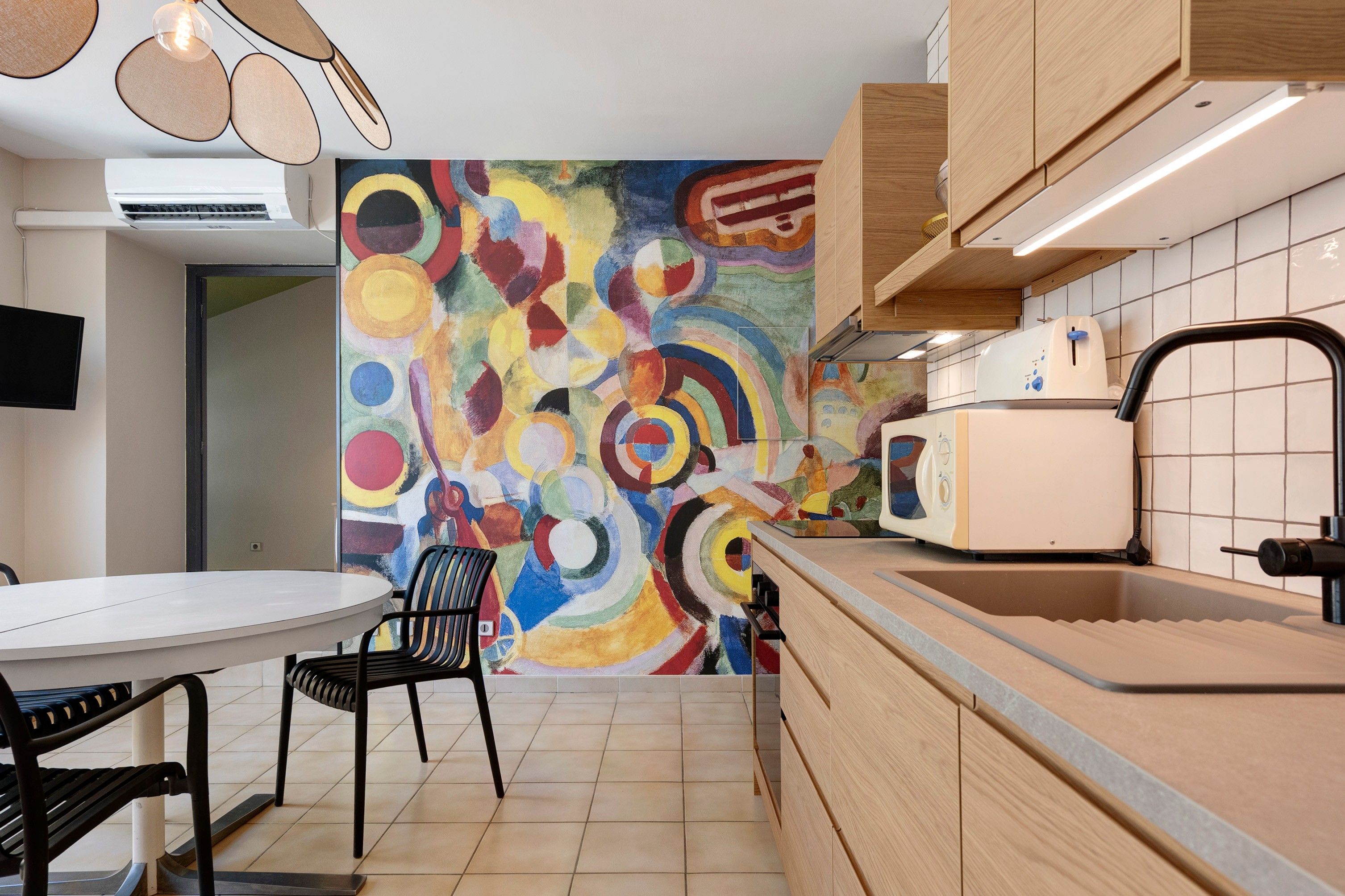 Een moderne keuken met een kleurrijke abstracte muurschildering, een eettafel met stoelen en een inbouwoven.
