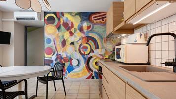 Een moderne keuken met een kleurrijke abstracte muurschildering, een eettafel met stoelen en een inbouwoven.