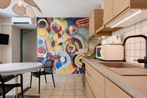 Une cuisine moderne agrémentée d’une fresque murale abstraite aux couleurs vives, une table à manger avec des chaises et un four encastré.