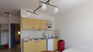 A compact kitchen with a microwave, sink, and cabinets, a wooden dining table, and a red trash bin. - Robert Delaunay Gîte with Wi-Fi in Vallon-Pont-d'Arc (Vallon-Pont-d'Arc)