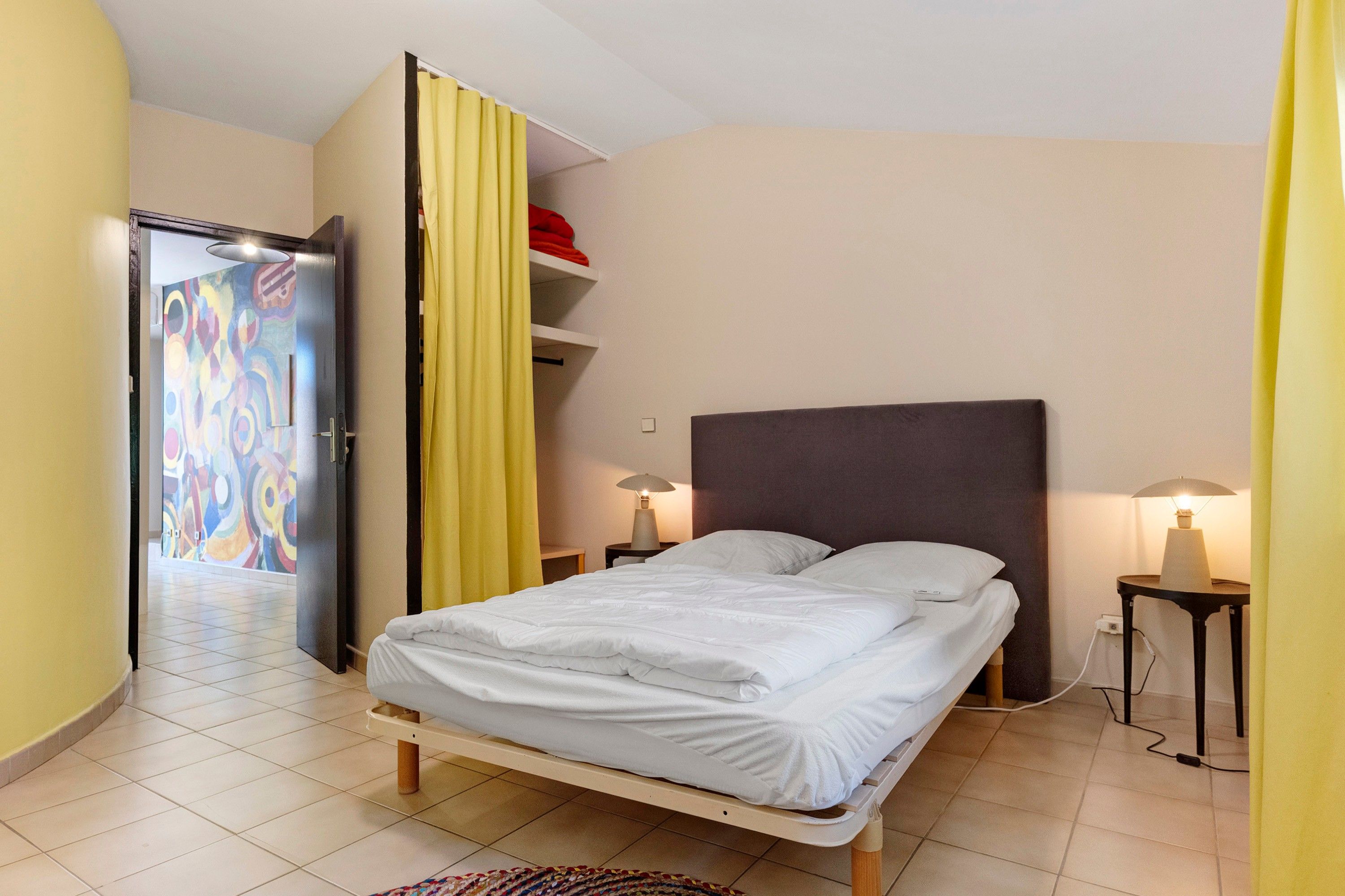 Una camera da letto con un letto, due lampade ai comodini, un armadio e una porta con un dipinto astratto dai colori vivaci.