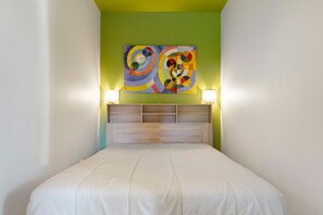 Une chambre d’hôtel avec un lit, une tête de lit dotée d’étagères et une peinture abstraite aux couleurs vives accrochée au mur.