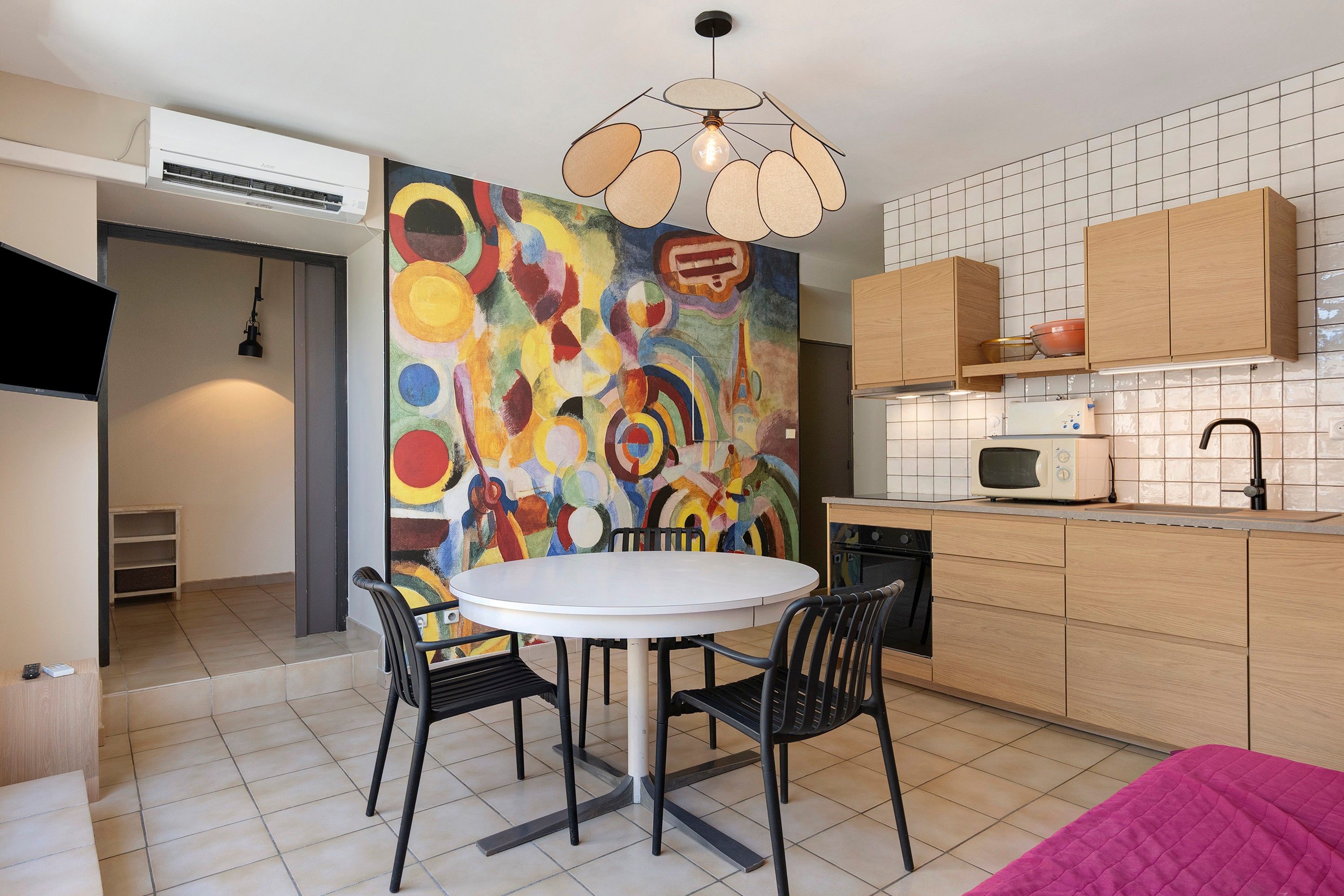 A modern kitchen with a round dining table, black chairs, and a colorful abstract painting on the wall.