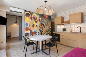 Een moderne keuken met een ronde eettafel, zwarte stoelen en een kleurrijk abstract schilderij aan de muur.
