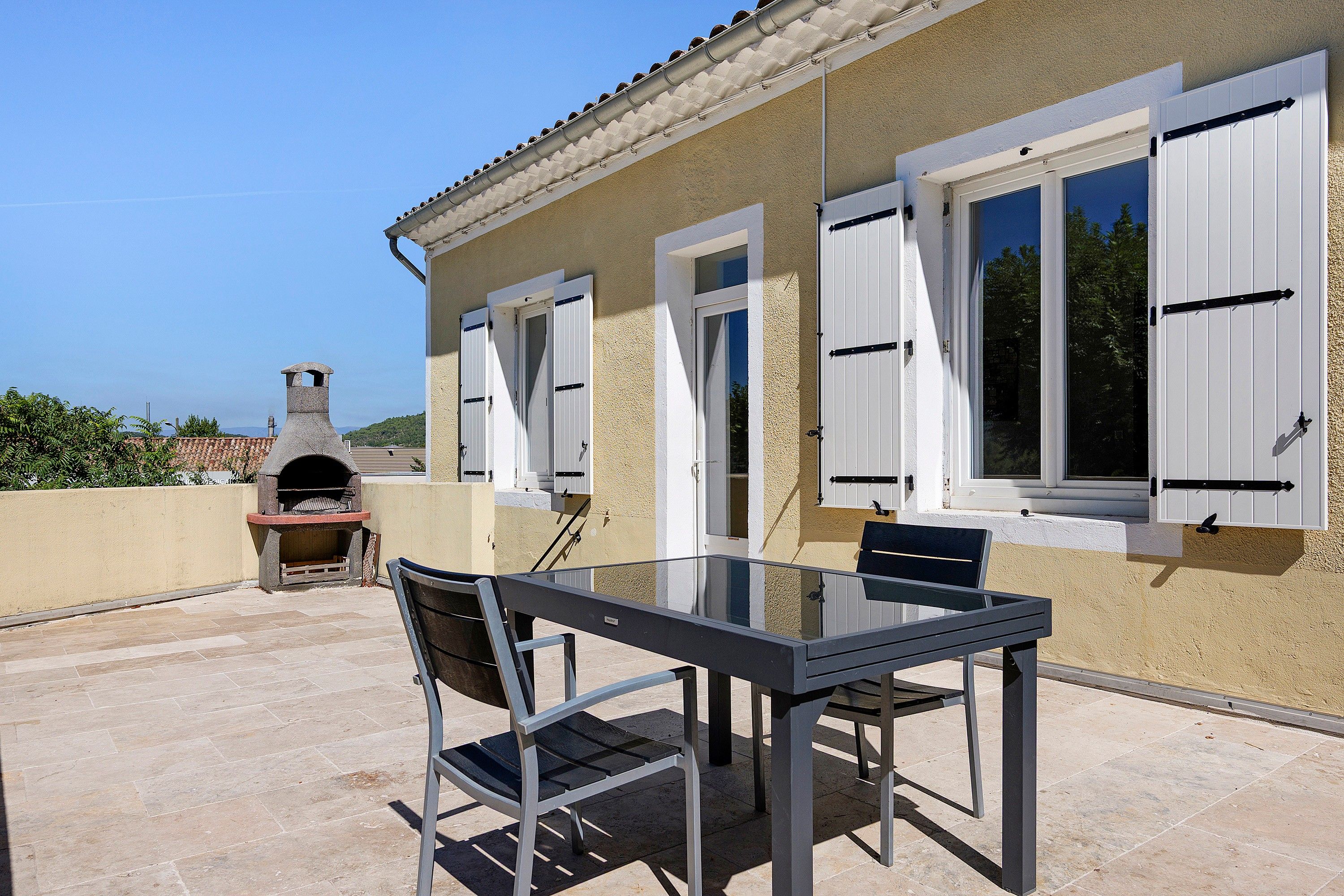 Une terrasse extérieure avec une table et des chaises, un four en pierre et une vue sur la mer.