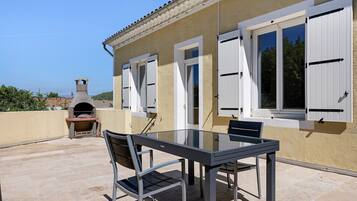Une terrasse extérieure avec une table et des chaises, un four en pierre et une vue sur la mer.