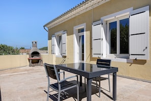 An outdoor patio with a table and chairs, a stone oven, and a view of the sea.