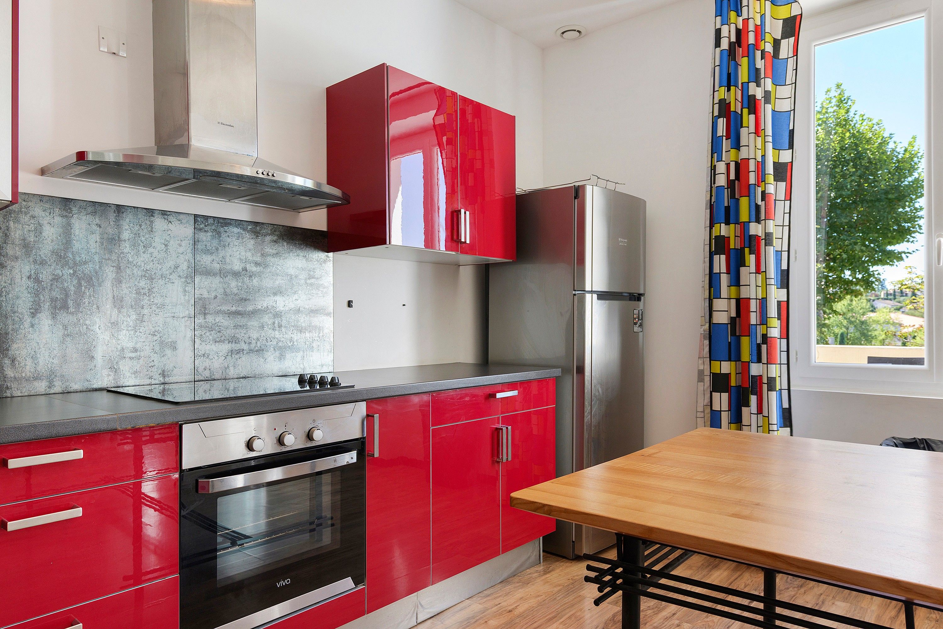 Une cuisine moderne avec des meubles de rangement rouges, un réfrigérateur en acier inoxydable et une table à manger en bois.