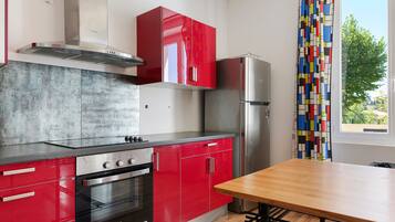 Une cuisine moderne avec des meubles de rangement rouges, un réfrigérateur en acier inoxydable et une table à manger en bois.