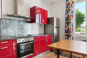 A modern kitchen with red cabinetry, a stainless steel refrigerator, and a wooden dining table.
