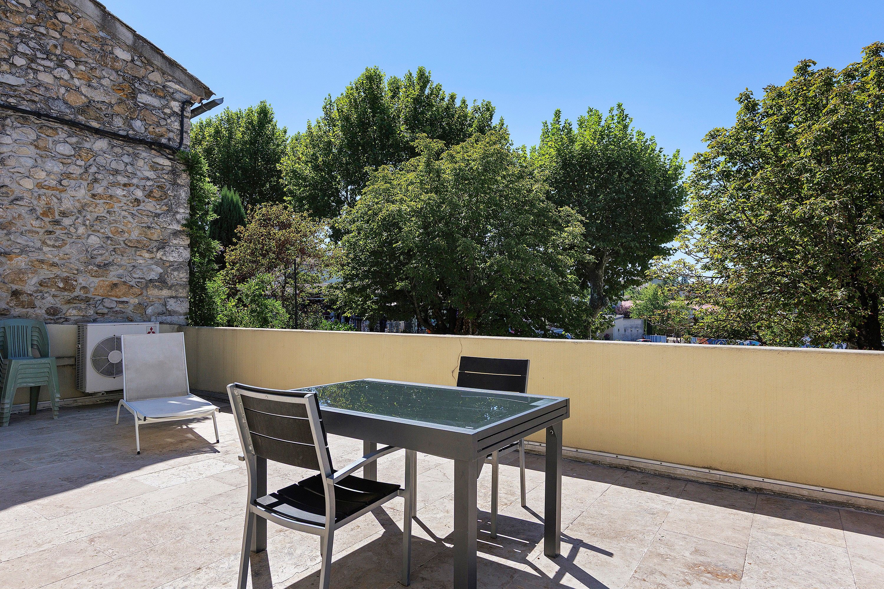 Un espace extérieur aménagé avec une table et des chaises, un mur en pierre et des arbres en arrière-plan.