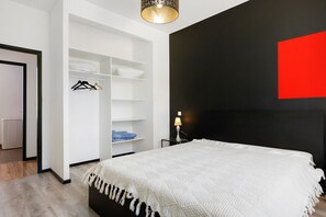 Quarto com cama, guarda-roupa, mesa de cabeceira e uma parede de destaque vermelha.