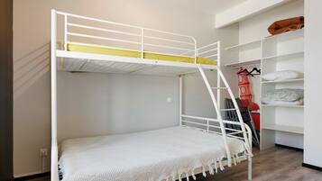 Un lit superposé avec une structure blanche et un matelas jaune. Il y a une couverture blanche sur le lit du bas.