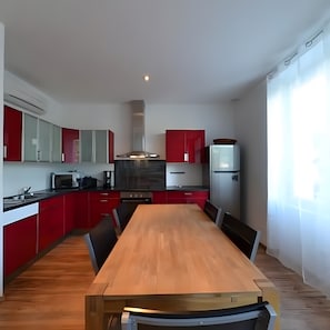Een moderne keuken met rode kastjes, een houten eettafel en een inbouwoven.