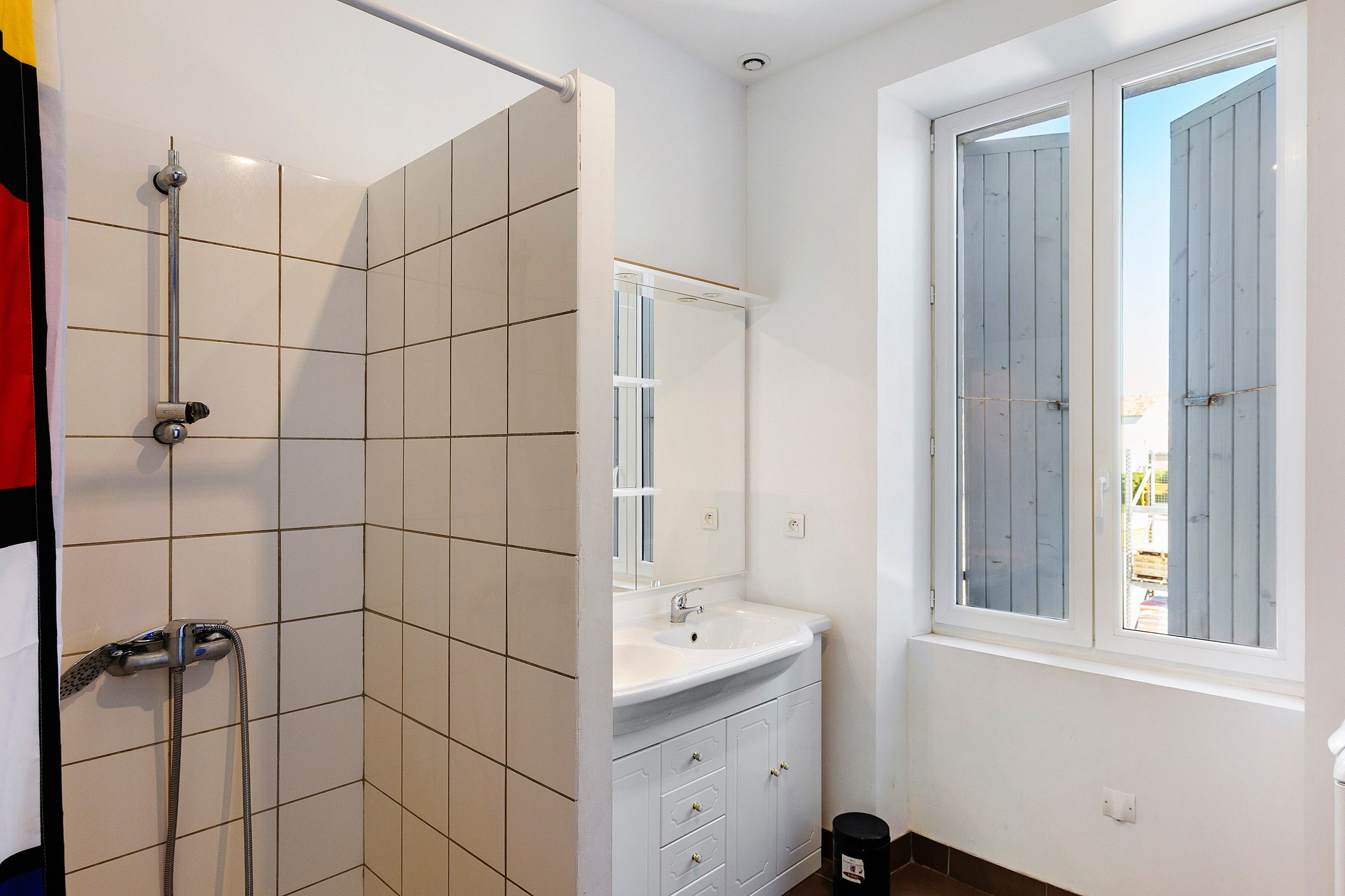 Een badkamer met een douche, wastafel en raam.