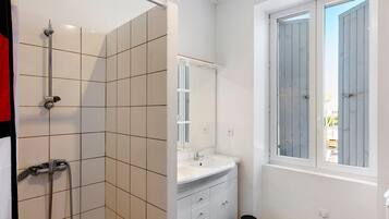 Een badkamer met een douche, wastafel en raam.
