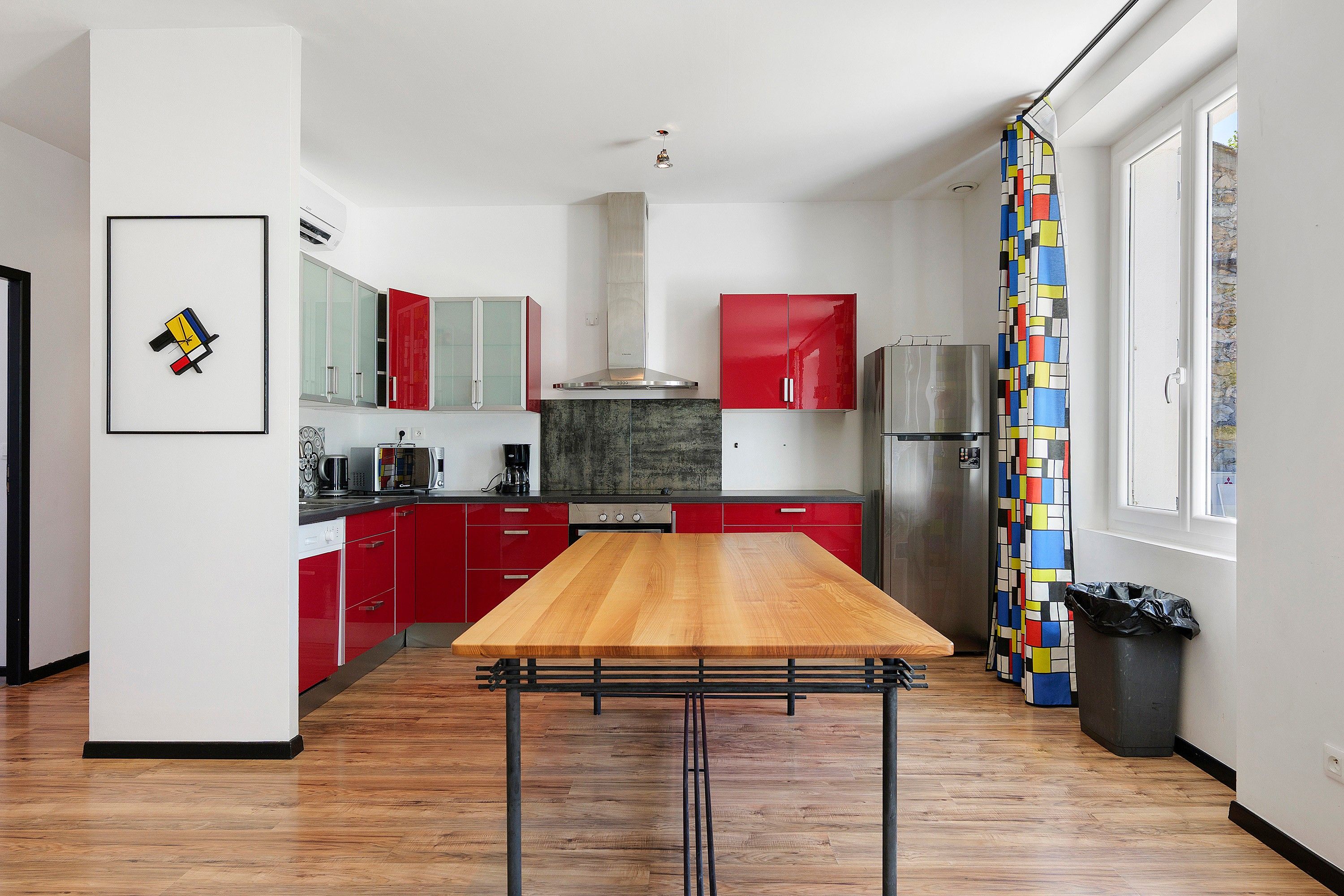 Una cucina moderna con un tavolo di legno, mobili rossi e un frigorifero in acciaio inossidabile.
