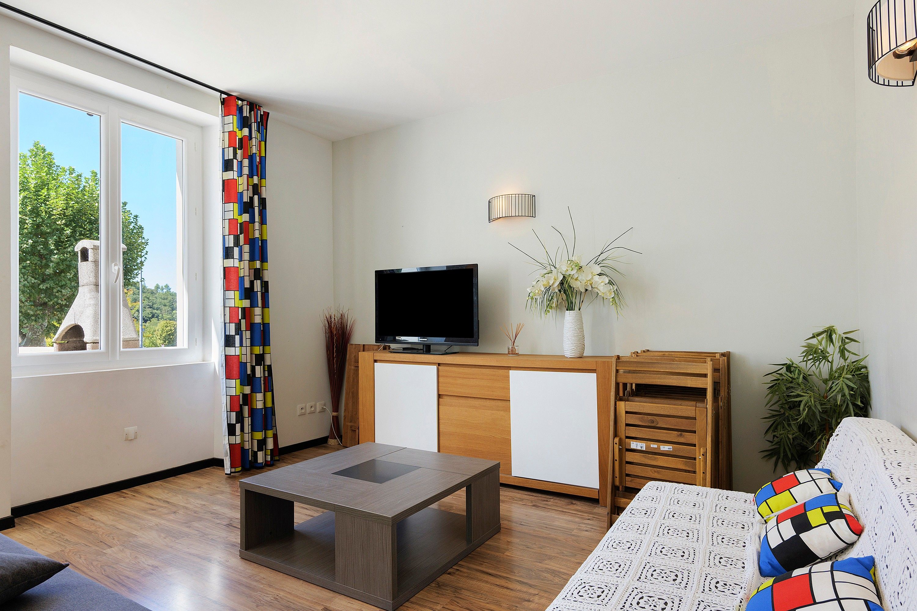 Een moderne woonkamer met een flatscreen televisie, een houten kast, een salontafel en een bank met decoratieve kussens.