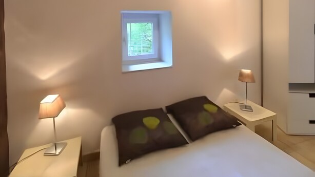 A bedroom with a bed, two bedside lamps, a small window, and a wardrobe. - Gîte '07' with Wi-Fi (Vallon-Pont-d'Arc)