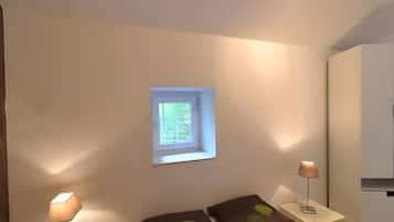 A bedroom with a bed, two bedside lamps, a small window, and a wardrobe.