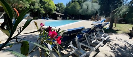 Un área junto a la piscina con sillones de descanso, una piscina y follaje circundante.