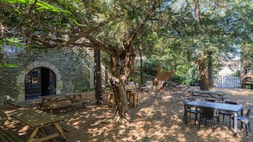 Un patio al aire libre con mesas de picnic y sillas, rodeado de árboles y un muro de piedra.