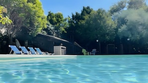 A swimming pool with clear water, surrounded by trees and a building with a covered area. - Gîte '07' with Wi-Fi (Vallon-Pont-d'Arc)