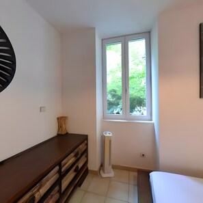 Una habitación con ventana, cómoda de madera, radiador blanco y cama.
