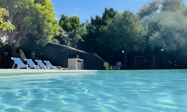 A swimming pool with clear water, surrounded by trees and a building with a covered area. - Gîte '03' with Wi-Fi (Vallon-Pont-d'Arc)