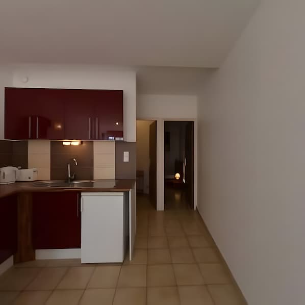 A modern kitchen with dark cabinets, a white refrigerator, and a tiled floor. - Gîte '03' with Wi-Fi (Vallon-Pont-d'Arc)