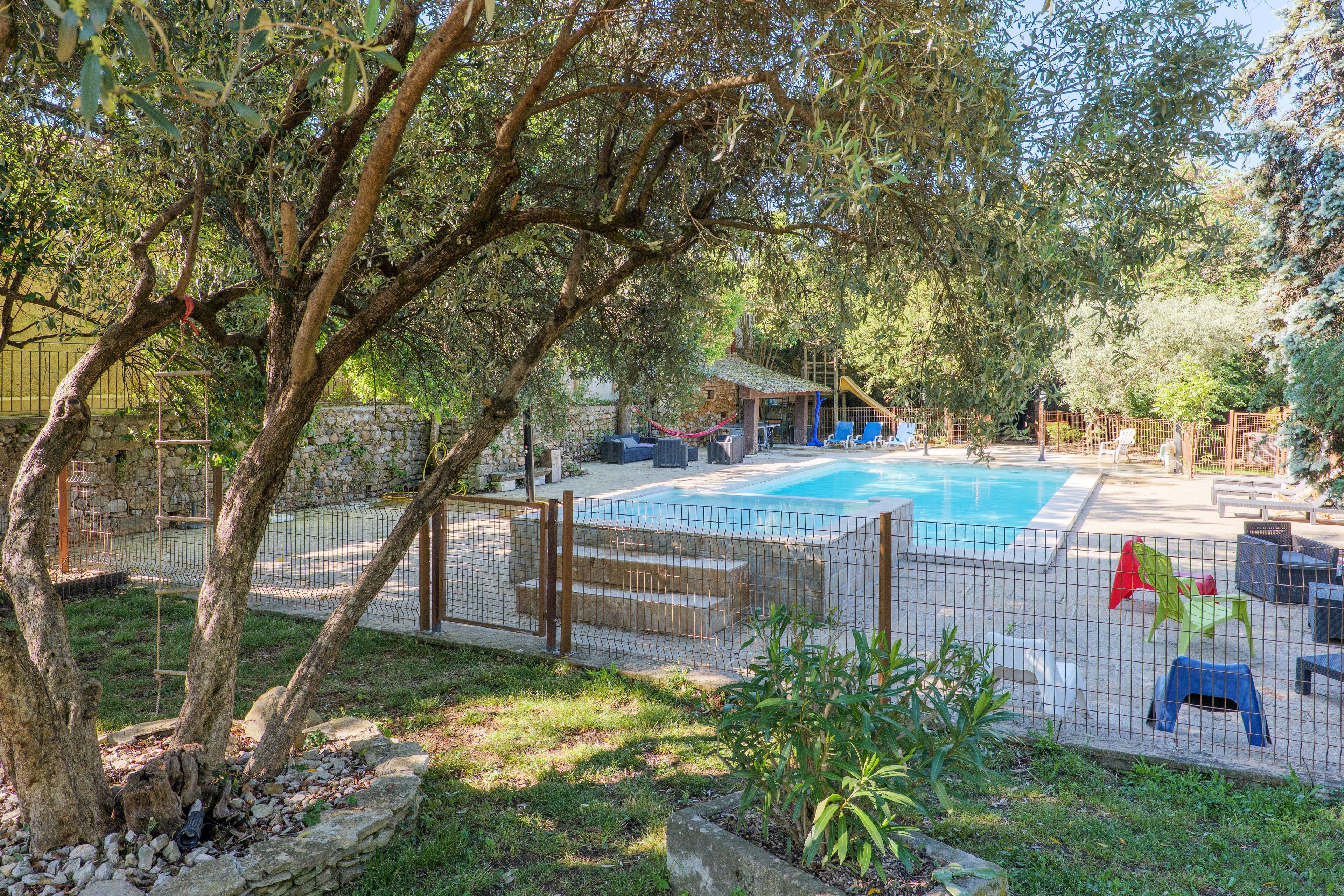 A pool area with a fenced deck, lounge chairs, and a small building in the background.