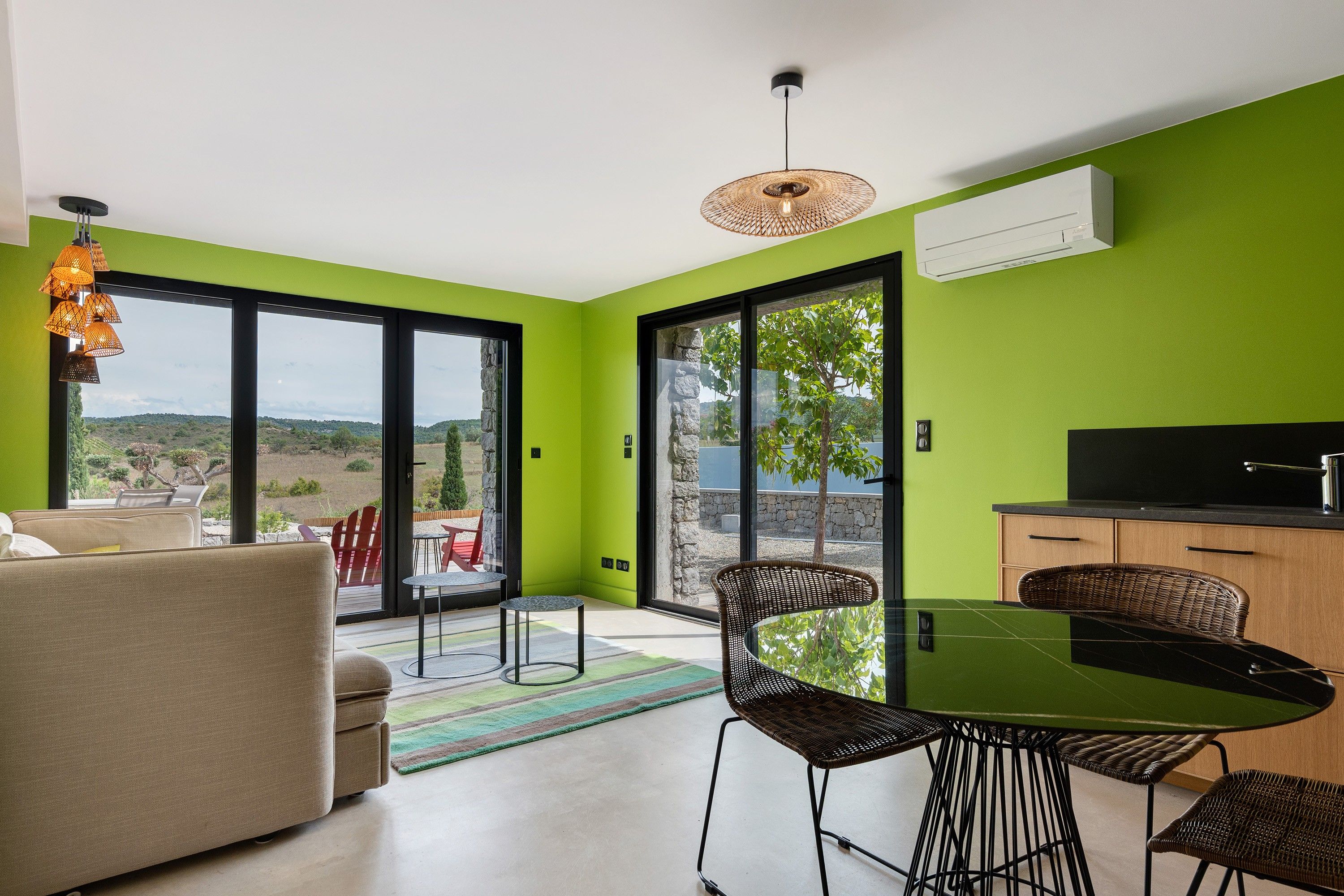 Een moderne woonruimte met een eethoek, een bank, een tafel en stoelen. Een groot raam biedt uitzicht op het omliggende landschap.