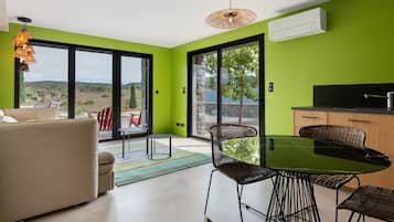 Een moderne woonruimte met een eethoek, een bank, een tafel en stoelen. Een groot raam biedt uitzicht op het omliggende landschap.