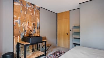 Een moderne slaapkamer met een groot bed, een houten garderobe, een zwarte wastafel op een houten tafeltje en een kleurrijk vloerkleed.