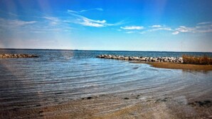 Una playa con aguas tranquilas, costa rocosa y cielo despejado.