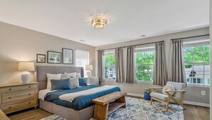 Un dormitorio con cama, mesitas de noche, un banco, una silla, una alfombra y un candelabro.