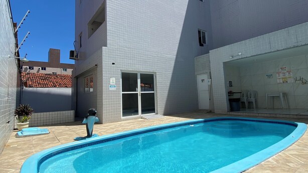 A swimming pool area with a tiled deck, a building with a tiled facade, and a clear blue sky. - Giza's Corner - Near Sol Beach (João Pessoa)