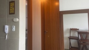 A hallway with a wooden door, a light fixture, a wall-mounted phone, and a sign. - Giza's Corner - Near Sol Beach (João Pessoa)
