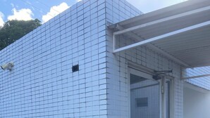 A building with a tiled exterior, a glass door entrance, and three waste bins labeled for plastic, glass, and metal recycling. - Giza's Corner - Near Sol Beach (João Pessoa)