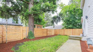 Un jardin avec une clôture en bois, un arbre et un chemin en béton.