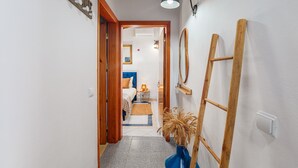 Ein Flur, der zu einem Schlafzimmer führt, mit einem Bett, einem Nachttisch, einer Lampe und einem Spiegel an der Wand.