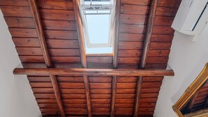 Eine Holzbalkendecke mit Dachfenster, einem Fenster und einer Wand-Klimaanlage.
