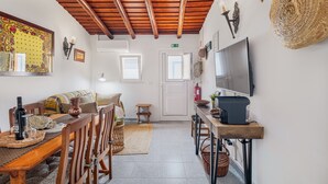 Ein gemütliches Zimmer mit Holzbalkendecke, einem Esstisch mit Stühlen, einer Couch, einem Fernseher und einer Küchenzeile mit Mikrowelle und Toaster.