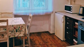 Eine kleine Küche mit Fenster, einer Mikrowelle, einem Kühlschrank und einem Esstisch mit Stühlen.