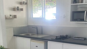 Eine kompakte Küche mit Spüle, kleinem Kühlschrank, Mikrowelle und einer Essecke mit einem Stuhl.