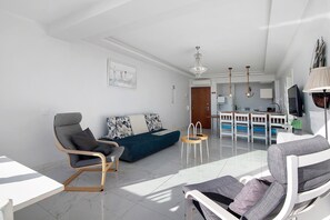 A modern living room with a sofa, chairs, a dining area, and a kitchen in the background. - Delmar Holiday Home with Sea View, Wi-Fi, and Air Conditioning (Quarteira)