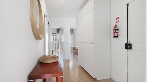Un pasillo con piso de madera, una mesa de madera con una cesta tejida, un espejo sujeto a la pared y un extintor.